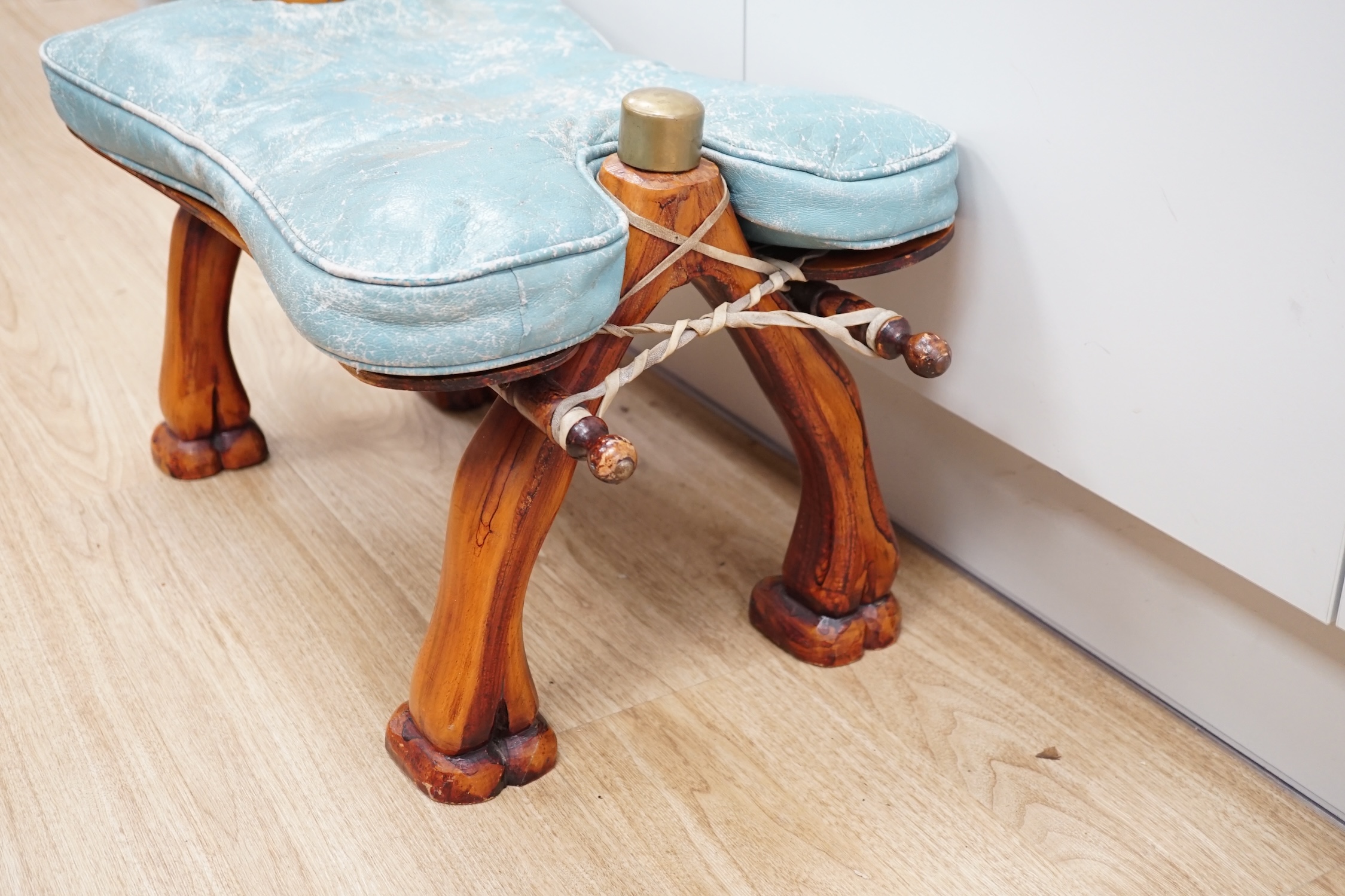 A carved wood foot stool in the form of a camel, blue stamped patterned leather cushion, 56cm high, 71cm wide. Condition - frame good, leather cushion worn